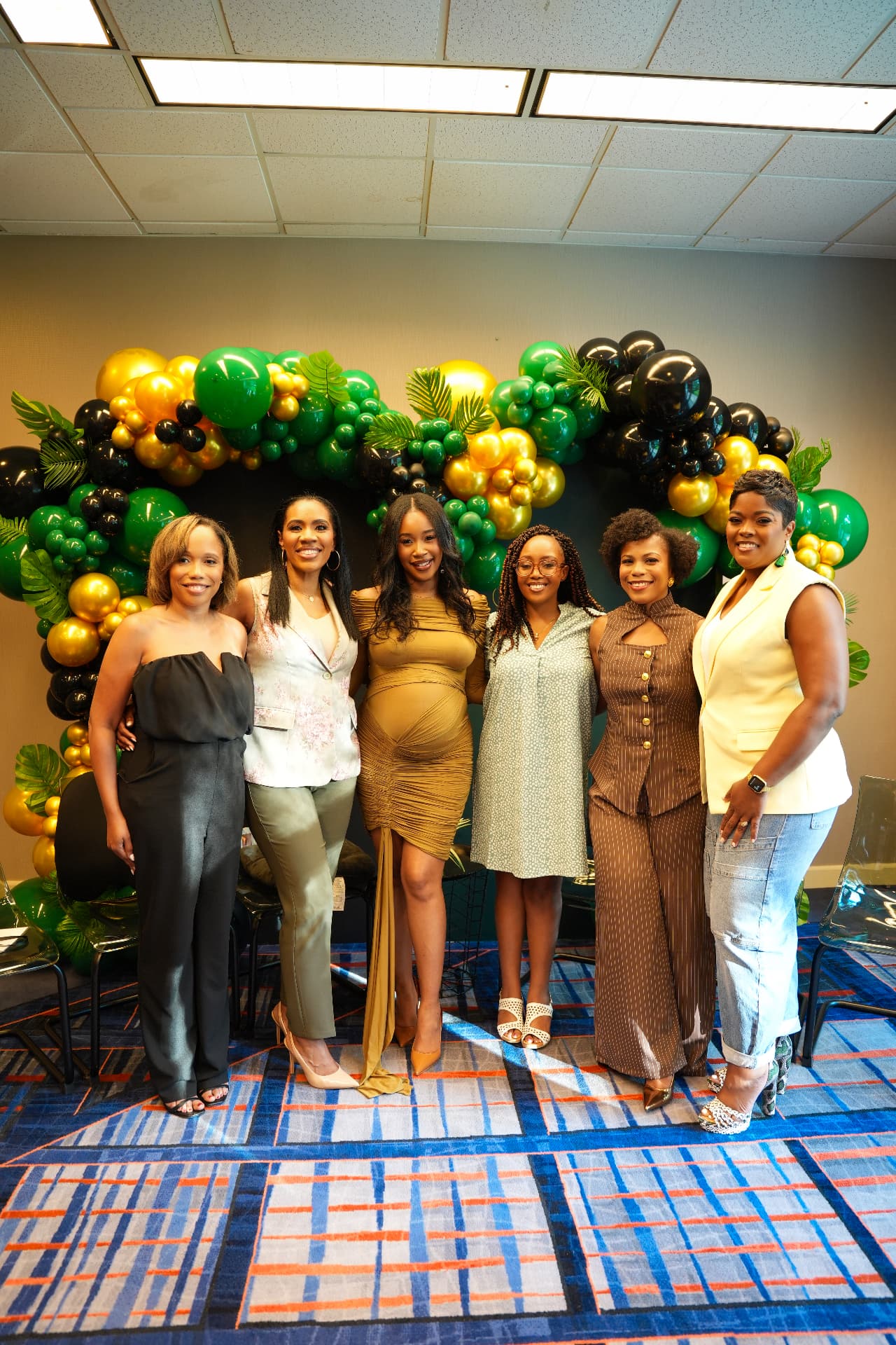 Six attendees posing beside the balloon and palm installation